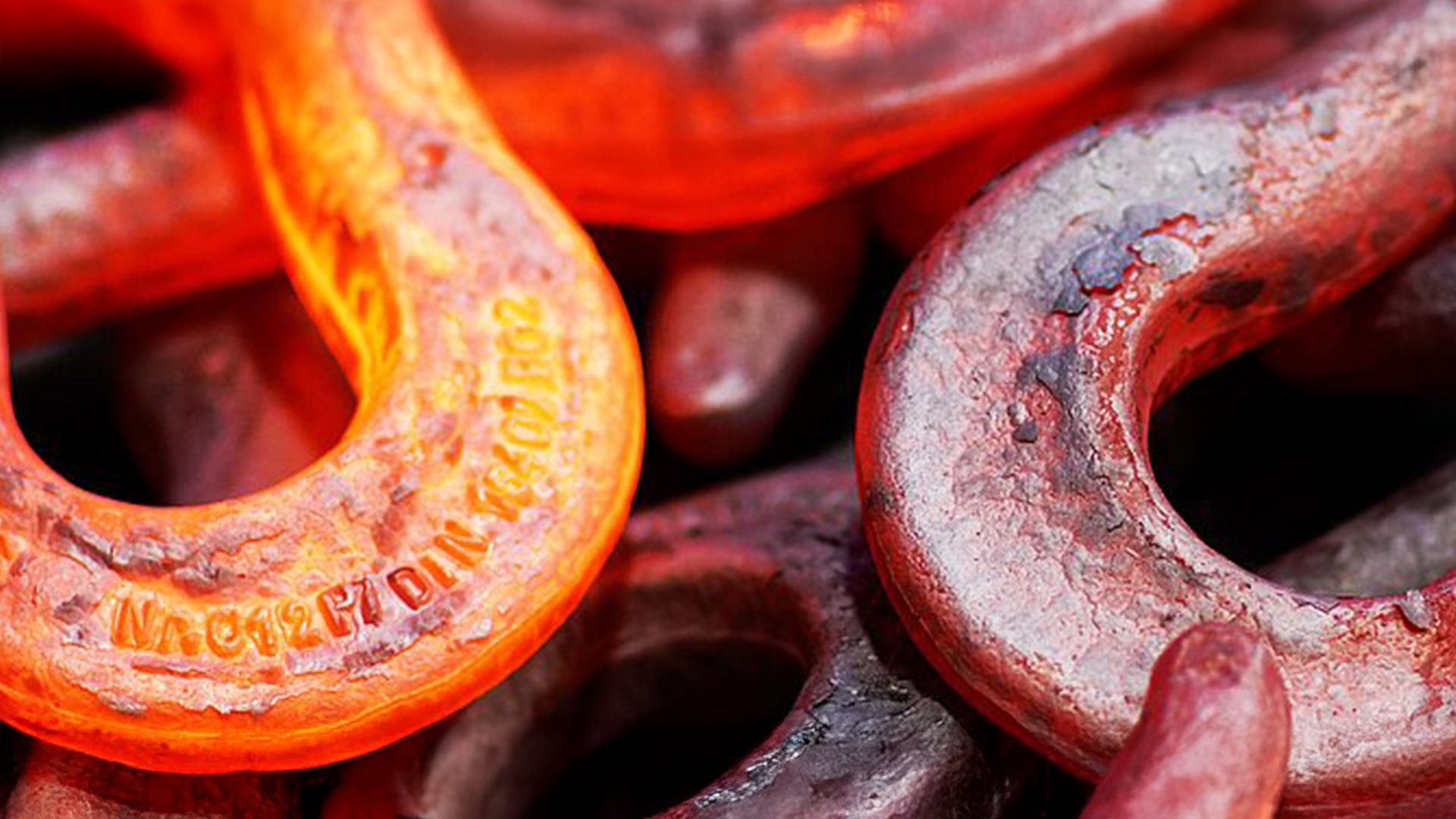 Nahaufnahme eines glühenden Lasthakens in rot-orange, Teil einer Metallverarbeitung.