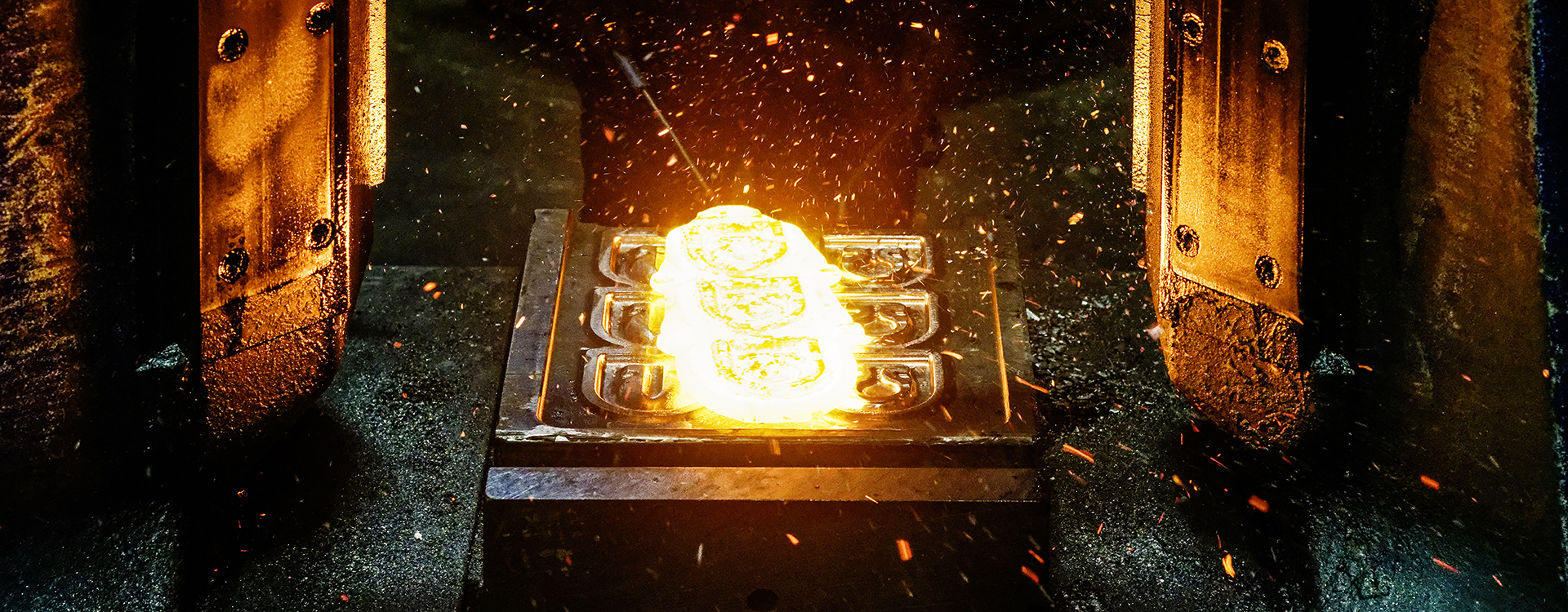 Glühend heißes Metall wird in eine Form gepresst, während Funken sprühen.